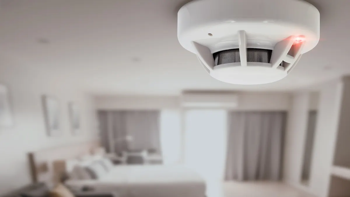 A carbon monoxide detector hangs above a hotel bed.