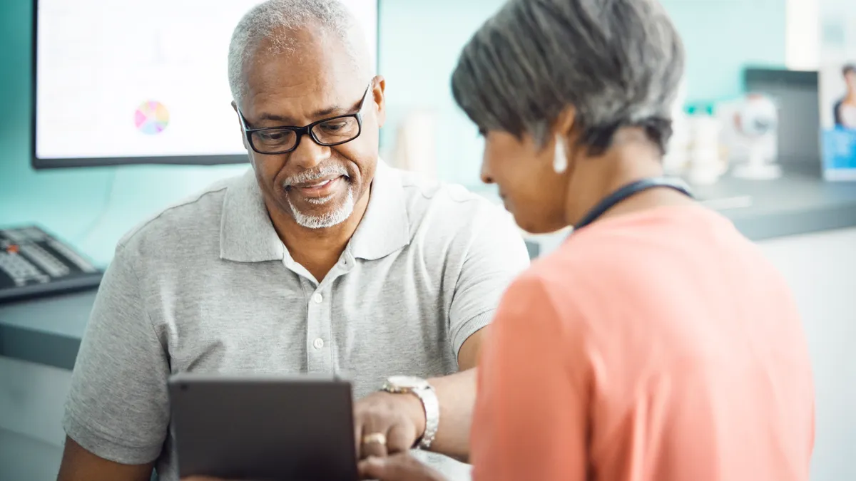 Male patient using tablet computer with female doctor in clinic