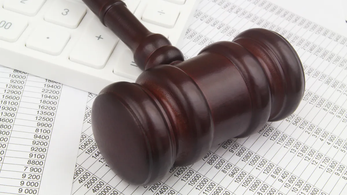 Wooden judge gavel and calculator on financial reports.