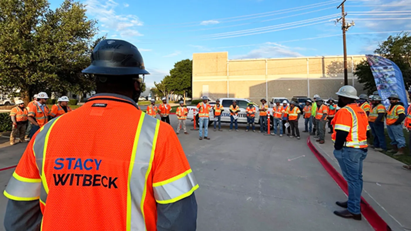 A group of construction workers stand for a discussion in a parking lot.