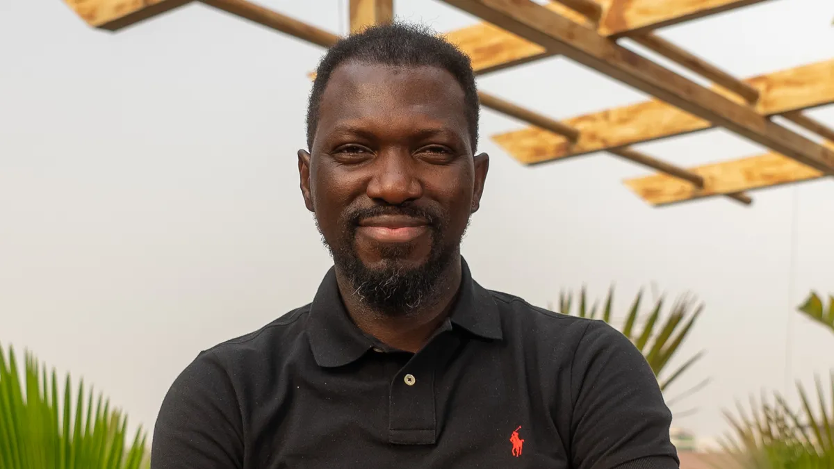 A man in a black polo wearing an apple watch with an orange band standing on a rooftop.