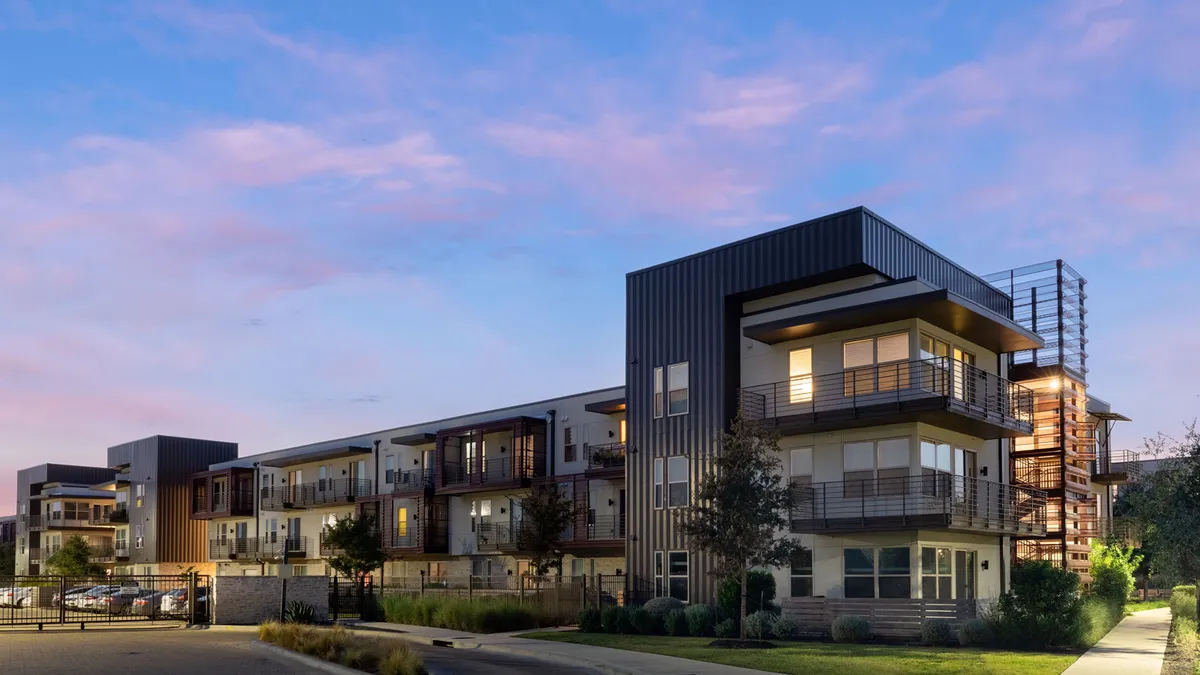 Three-story tan and dark modern apartment with wraparound balconies on the corners.