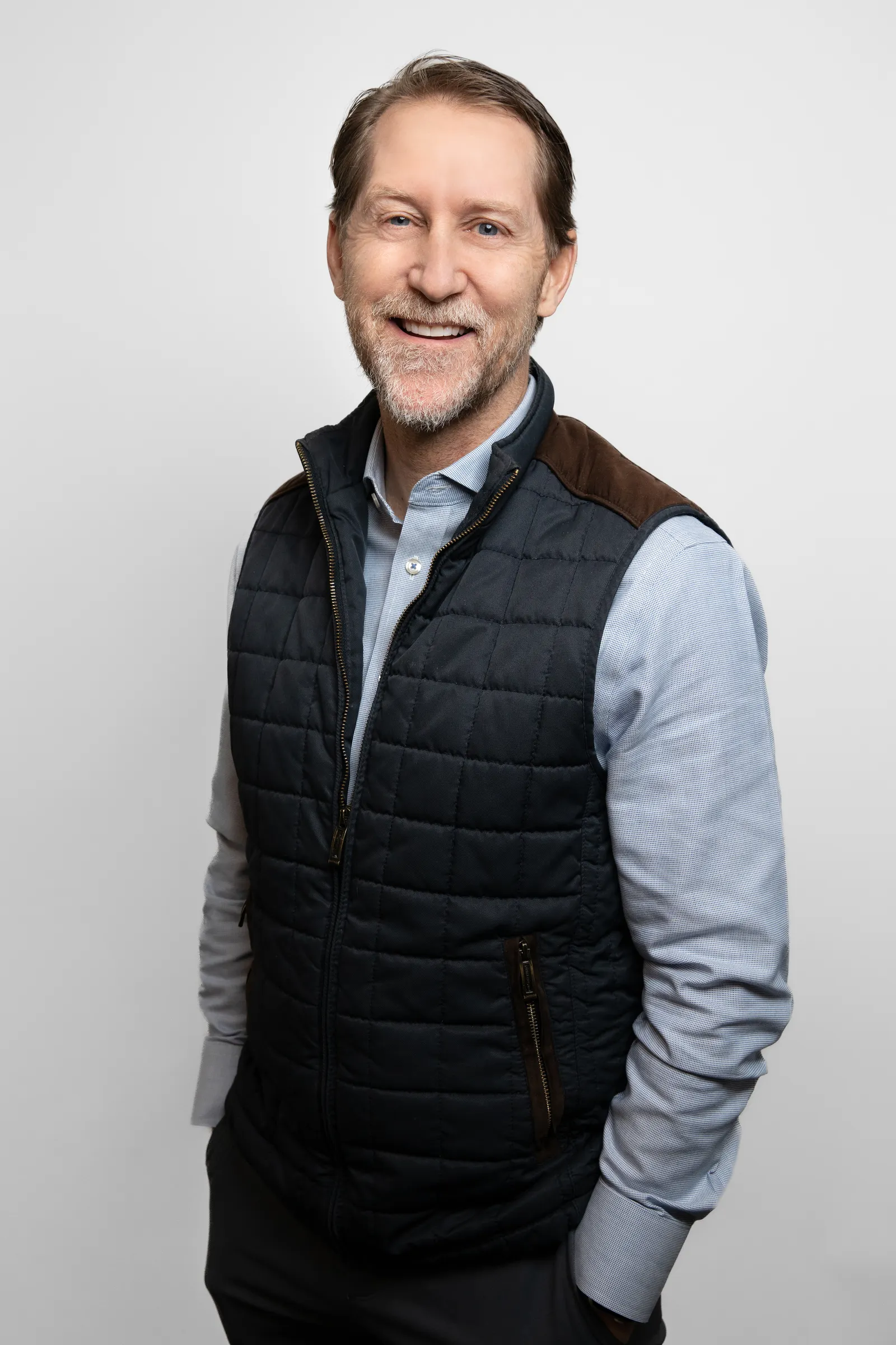 A person in a checked shirt and vest stands and looks straight ahead.
