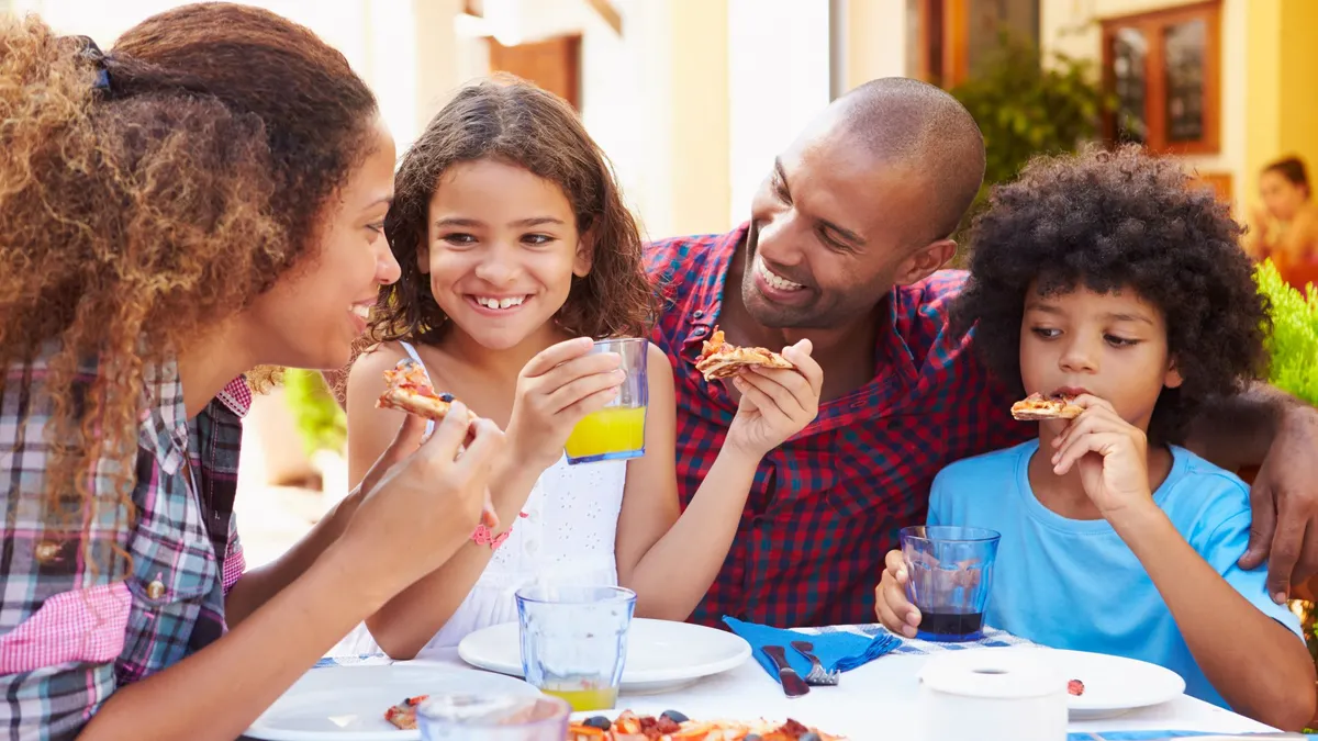 Two adults with two kids eats pizza at a restaurant.