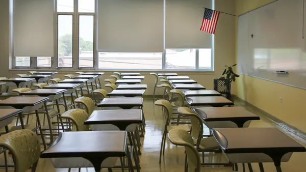 An empty classrooms with rows of desks and an American flag hanging near a chalkboard.