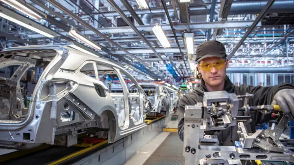 A man in a gray cap and jacket and yellow safety goggles working on a automotive component.