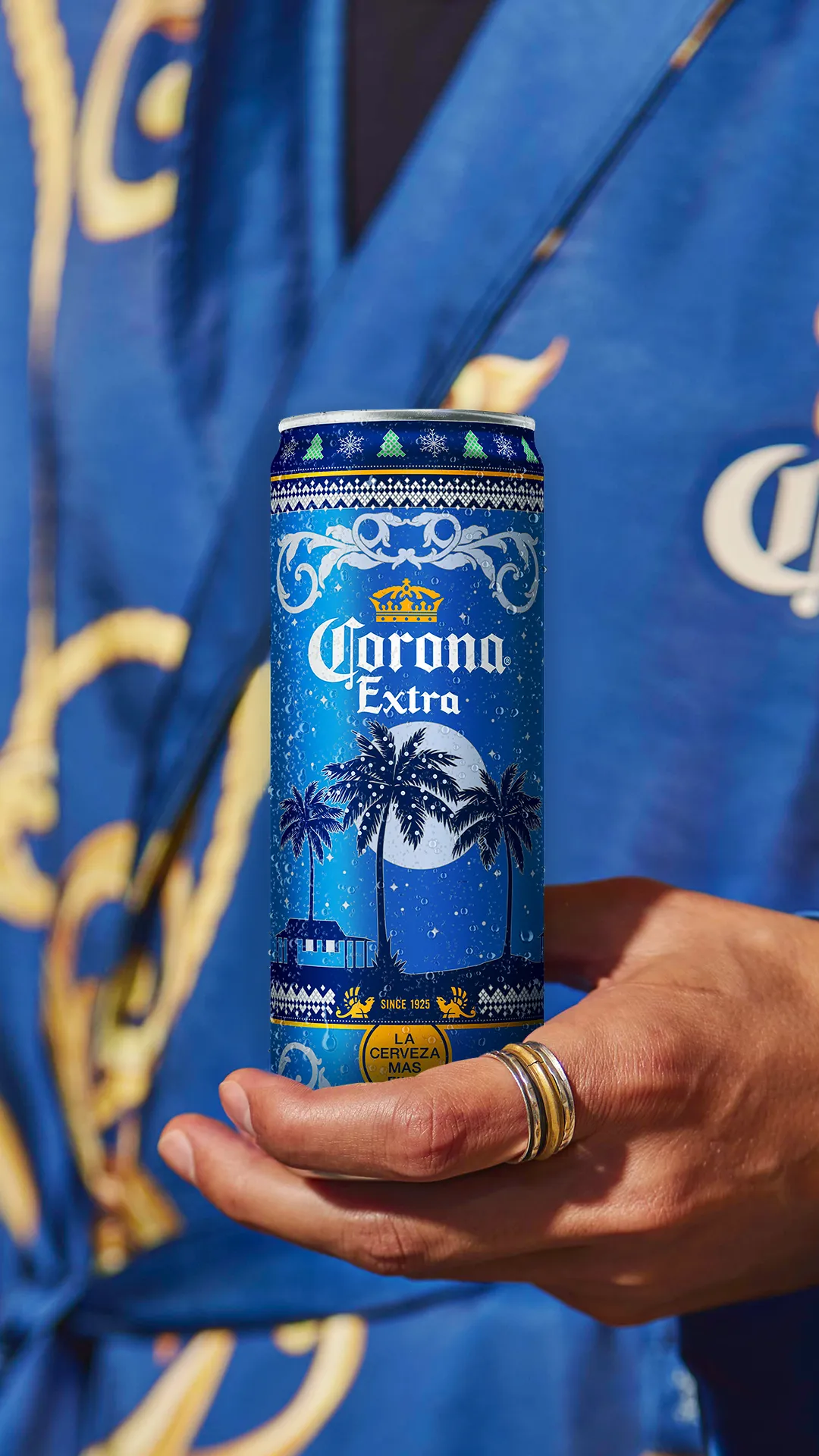 A person holding a can of Corona beer with a holiday design on the outer surface.