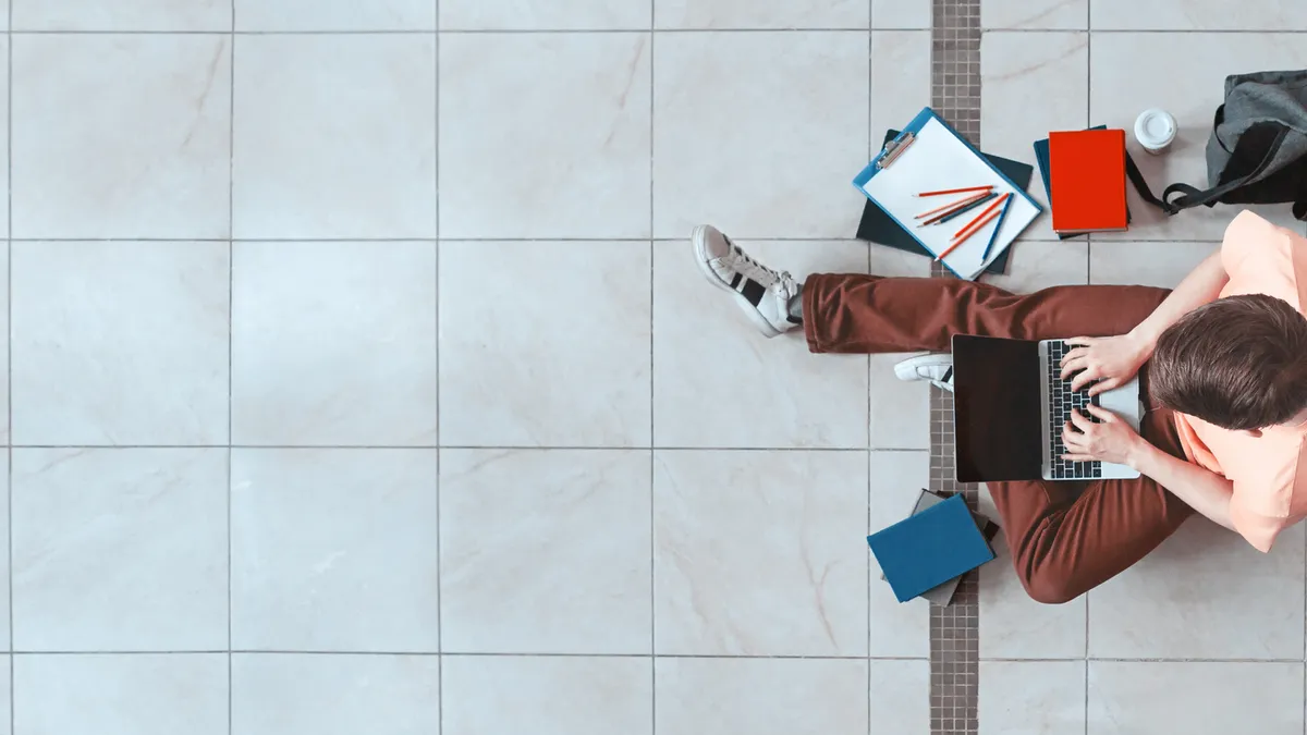 An aerial view of a student using a laptop while sitting on the floor.