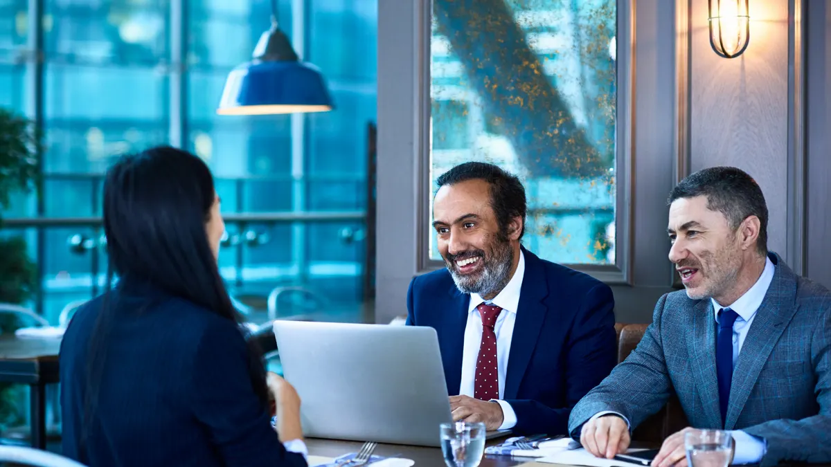 Mature professional males opposite younger businesswoman, smiling and cheerful, relaxed job interview