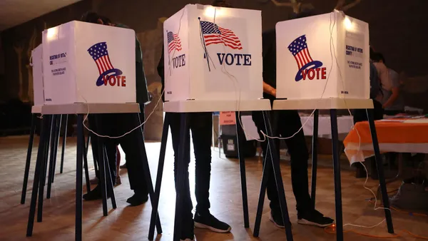 three people stand behind voting booths