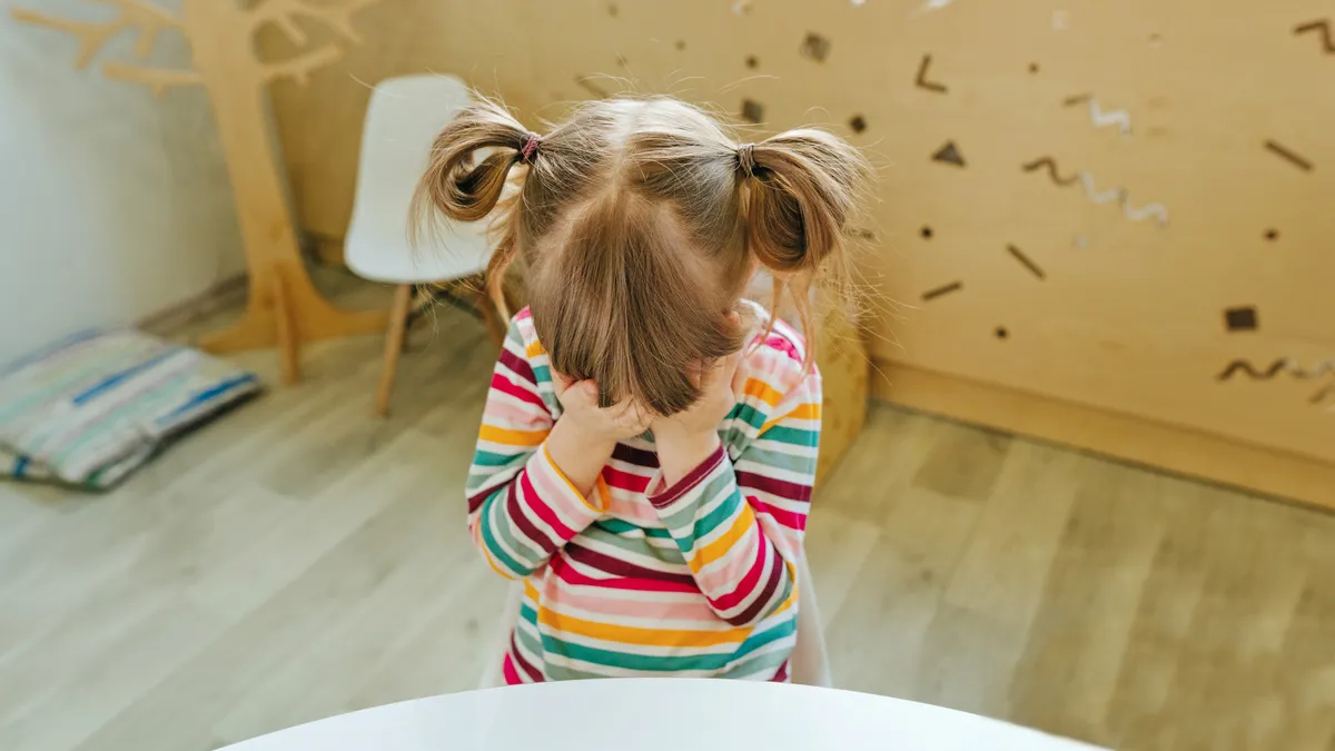 A young student sits at a classroom table with head in hands.