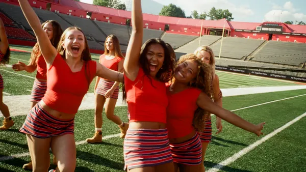 A group of girls in matching red cropped tanks and stripped skirts pose in a football field.