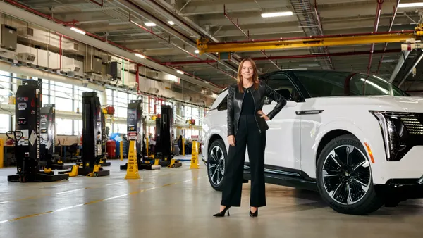 Mary Barra, General Motors Chair and Chief Executive Officer pictured stand in front of a Cadillac Escalade SUV in a dealership service facility..