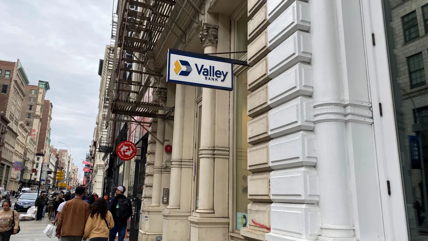 People walk on a sidewalk past an entrance with a "Valley Bank" sign above the doorway.