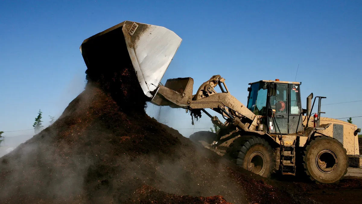 A tractor dumps organic material onto a large pile of organic material.