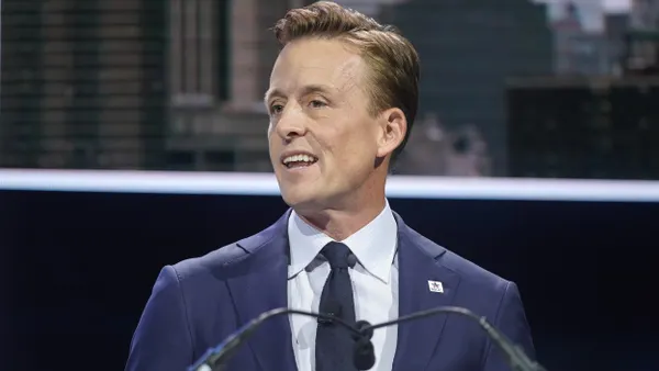 Sean Cairncross stands on a stage in front of two microphones
