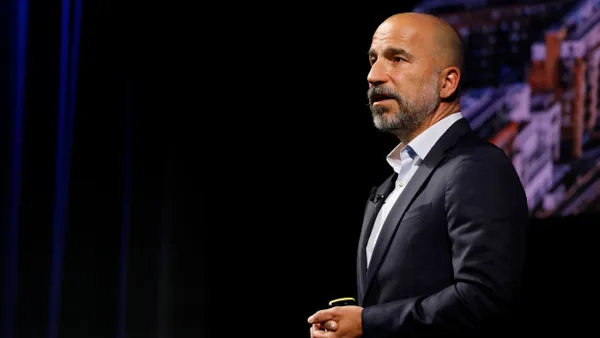 Bald man in dark suit seen from his left side standing on a dark stage.