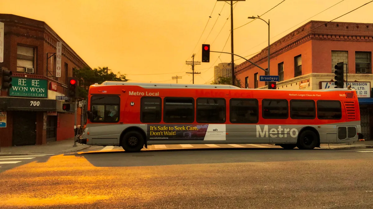 A red and gray Los Angeles Metro bus is driving through an intersection along Broadway in downtown LA.