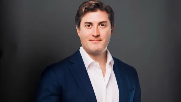 A head and shoulders shot of a person in a dark suit against a gray background.