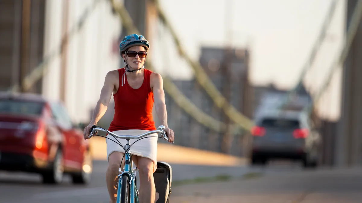 A person with a helmet and sunglasses rides a bike in front of blurred out streetscape.