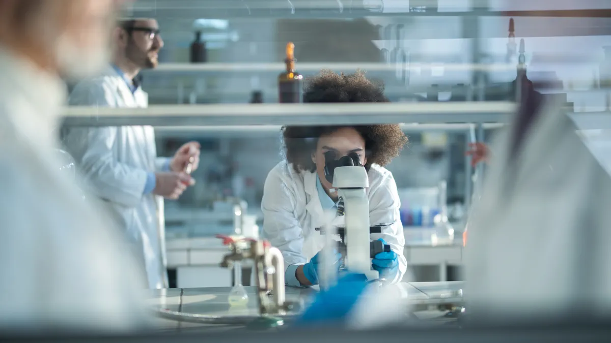 Young African American biochemist using microscope while working on scientific research in a laboratory. The view is through the glass.