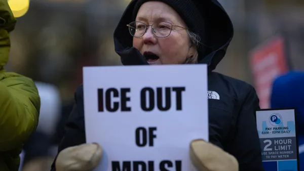 A person wearing winter coat and gloves holds a sign that says "ICE OUT OF MPLS!"