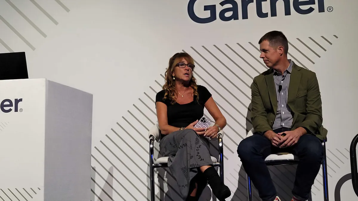 Cindy Taibi speaks onstage, sitting next to Joe Wilson, against a white backdrop with Gartner signage.