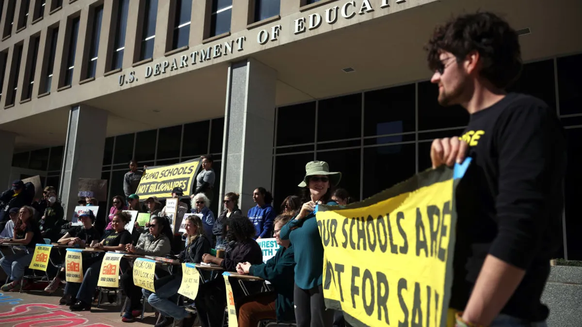 A group of people are standing outside the U.S. Department of Education with signs