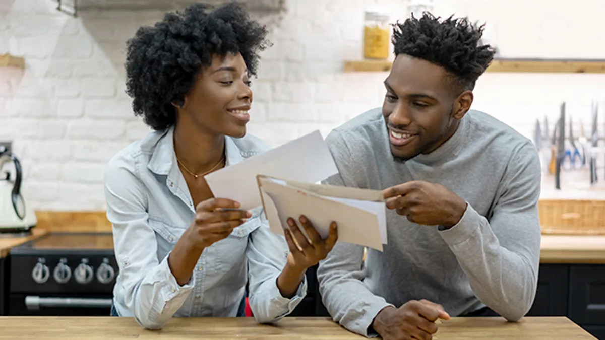 Two people smiling and leaning forward on counter looking through stack of papers.