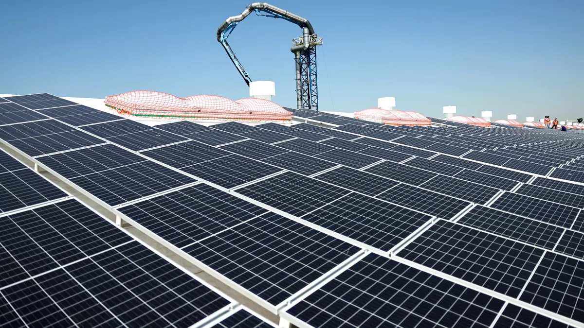 Workers stand between solar panels.