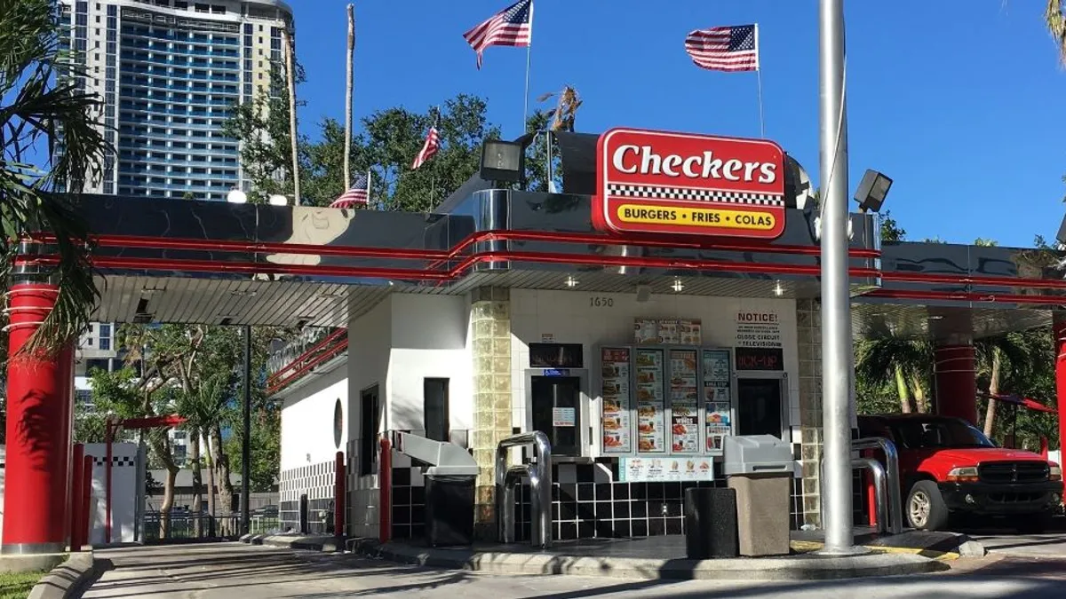 A Checkers restaurant with metallic and red trim and a red truck waiting for an order.