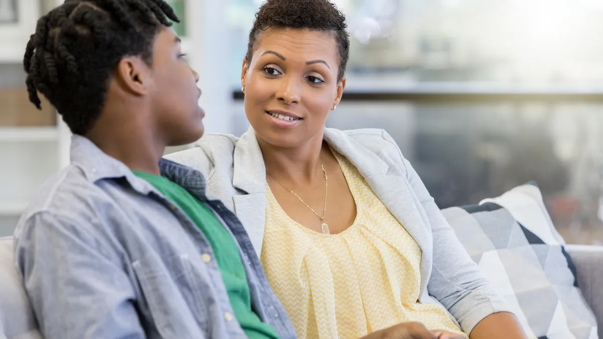 An adult and older student sit on a couch while the student speaks, the adult listens.