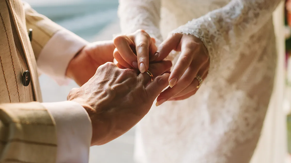 Person in a wedding dress puts a ring on someone's finger.