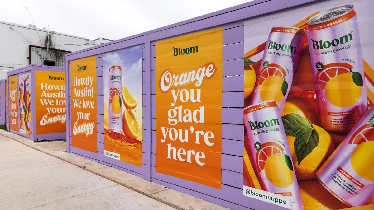 Posters advertising Bloom's energy drinks are displayed on a purple fence.