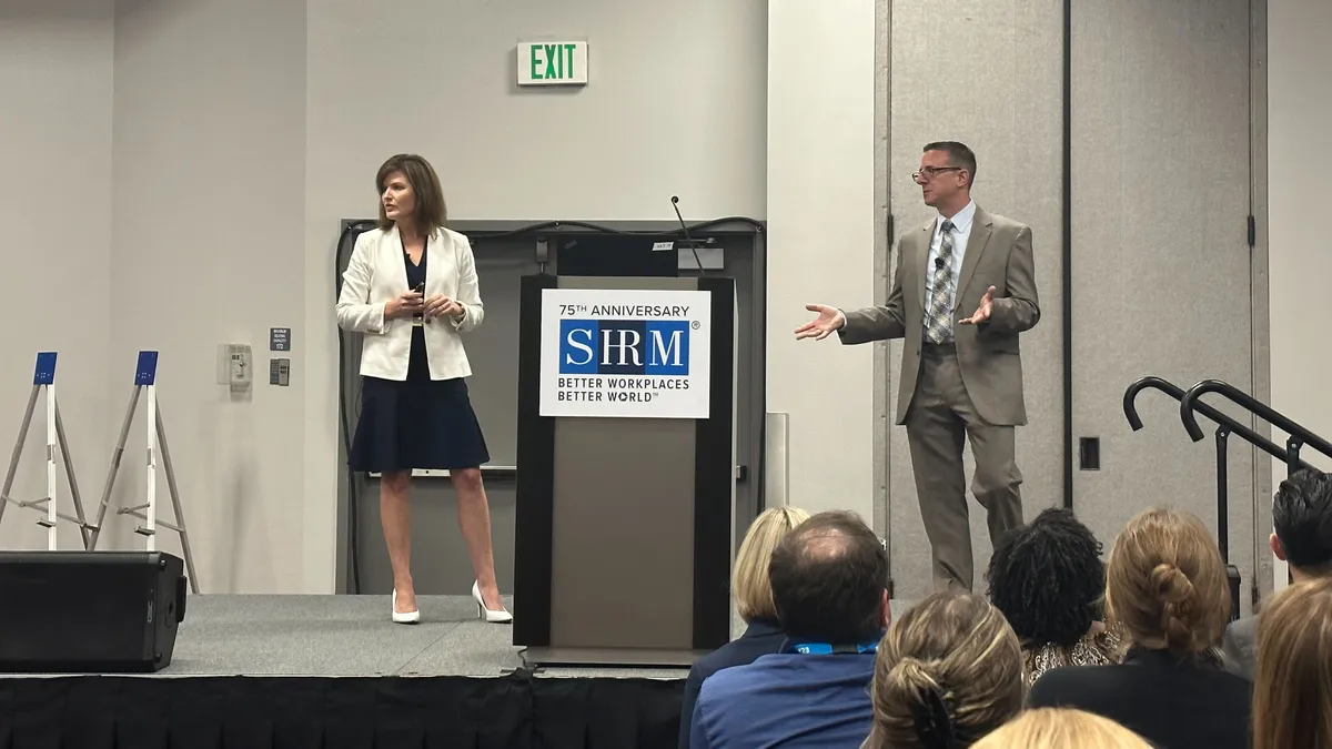 Two speakers present on a stage in a conference room.