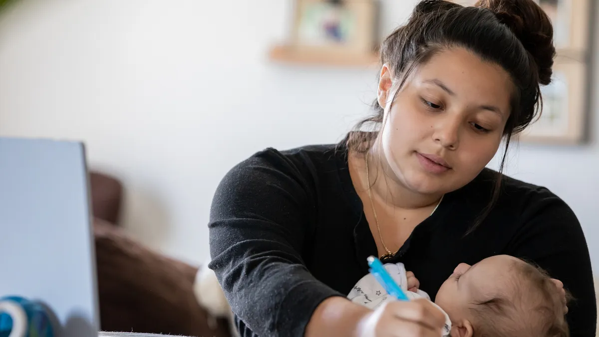 A person writes while holding a baby.