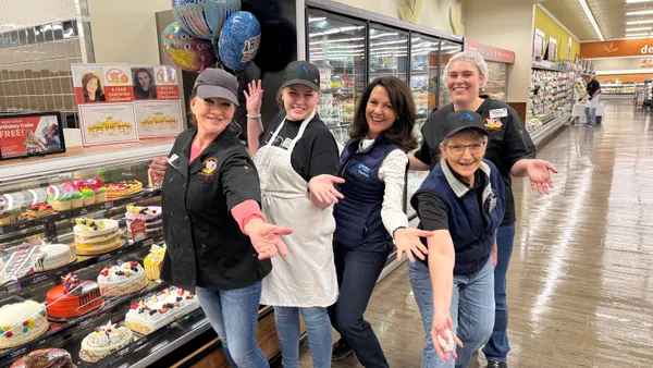 A group of people standing next to a bakery counter in a grocery store.
