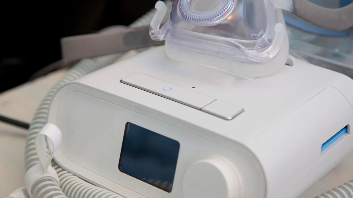 A rounded, white device sits on a table with a clear mask on top.