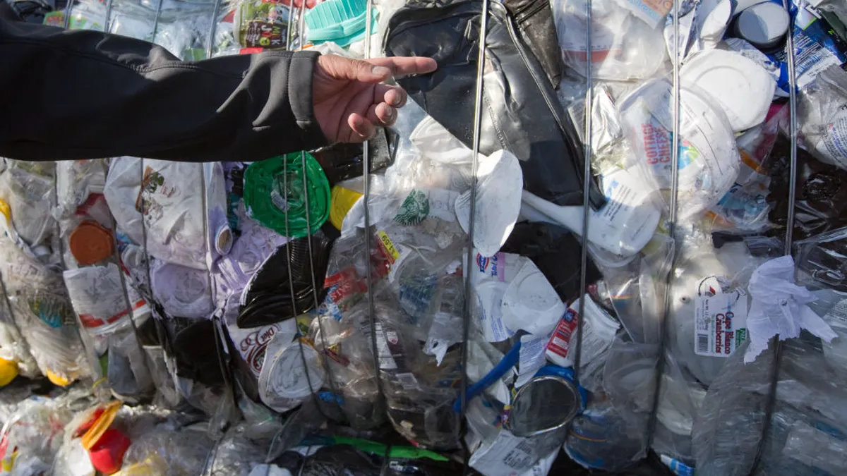 A person's hand points at a bale of plastic packaging collected for recycling