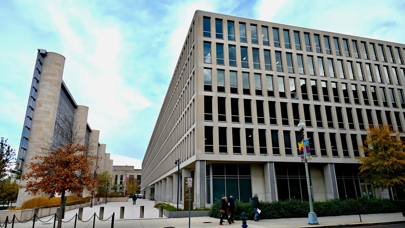 The outside of the U.S. Department of Education in Washington, D.C. is shown on a close day. People are walking on the sidewalk in front of the building.