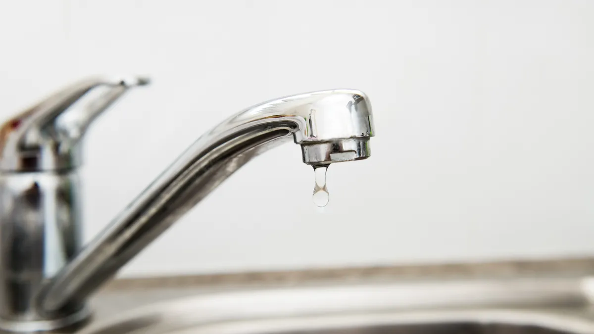 Selective focus on a modern stainless steel faucet on top of a leaking sink. The tap is dripping water.