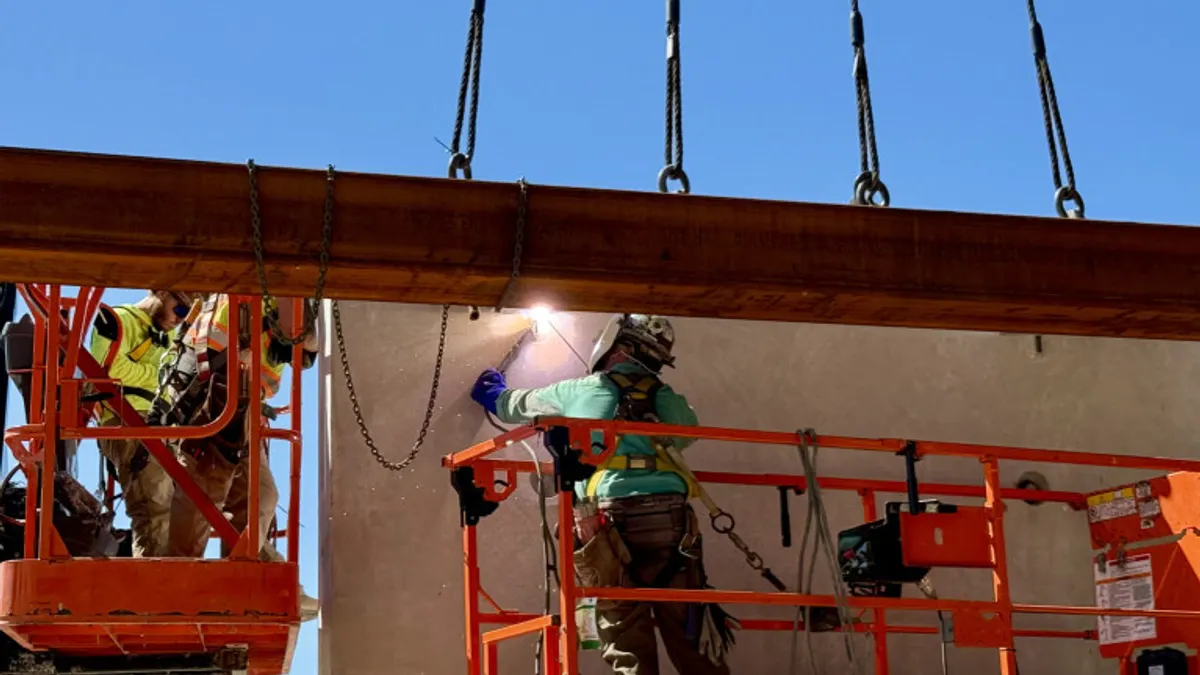 Construction workers on lifts work on equipment hoisted into place.