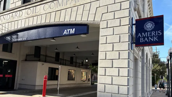 The corner of a stone building is shown from street level, with a sign showing the Ameris Bank name and lion logo mounted on the side of the building.
