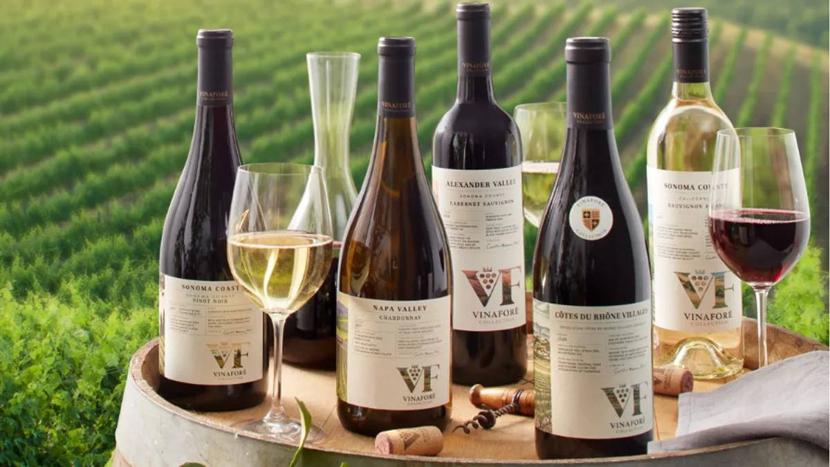 Wine bottles and glasses on a table outside with a vineyard in the backdrop