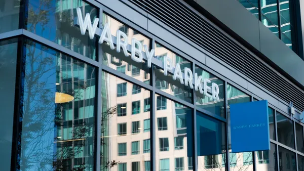 Reflections of buildings on a Warby Parker store window, dominated by white and blue.