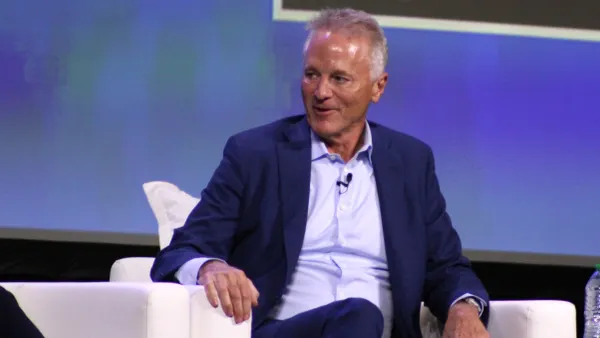 A person wearing a suit sits in a white chair.