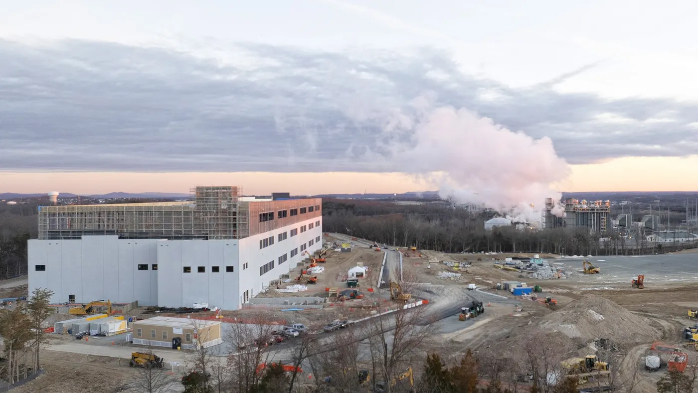 Steam rising from a power plant with construction equipment in the foreground.