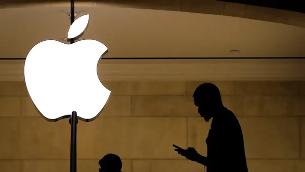 A man in shadow looks at his mobile device near a lit up Apple logo.