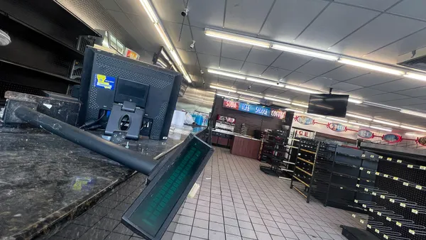 The inside of a convenience store with a broken cash register and empty shelves.