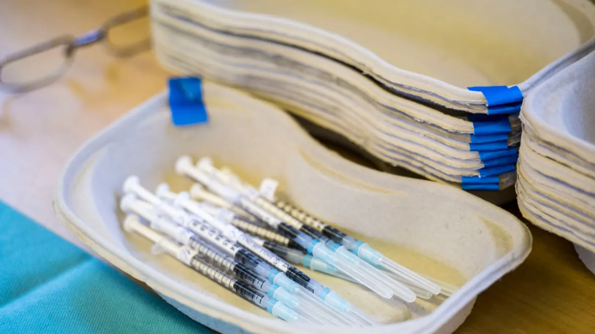 A handful of syringes containing COVID-19 vaccine doses rest in a cardboard tray.